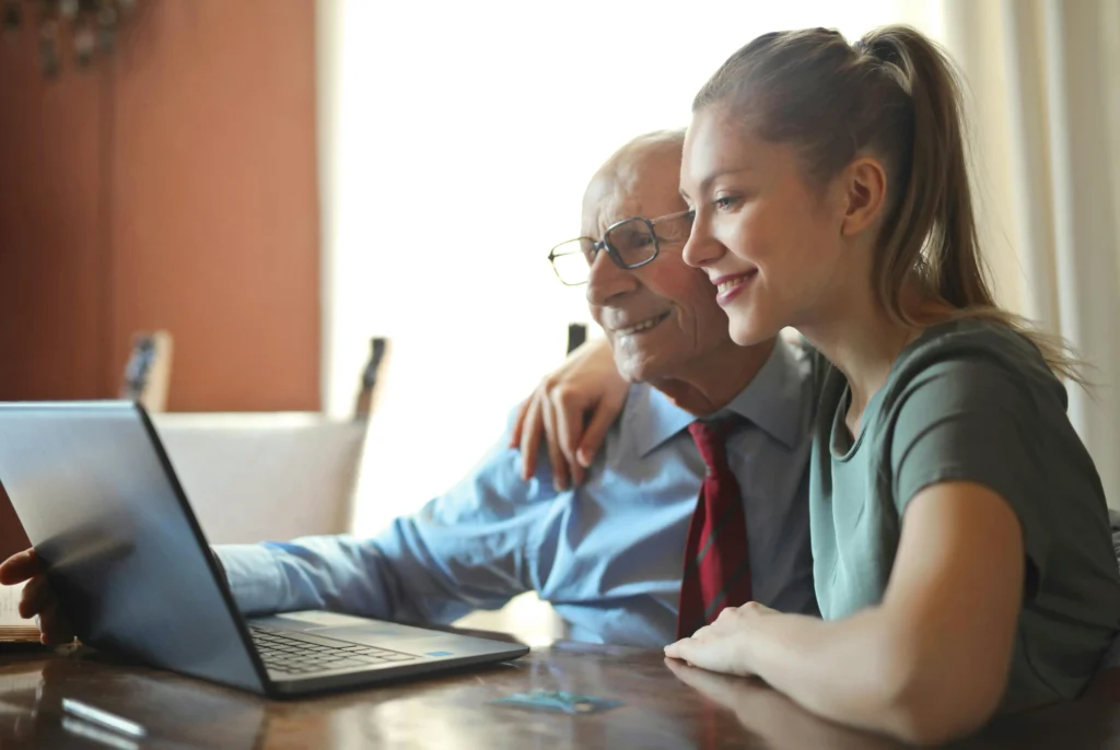 Abuelo y nieta sentados juntos frente a una computadora, revisando documentos en línea.