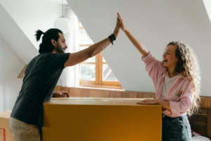 Una pareja sonriendo y chocando las manos mientras desempacan en su nuevo hogar, gracias a un apadrinamiento de parejas.